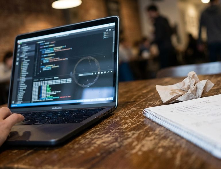 On-site Coffee shop working environment: a laptop open on a scratched wooden table, screen showing